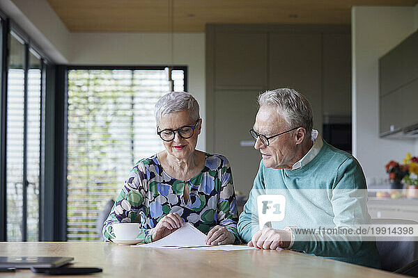 Senior couple sitting at table at home examining document