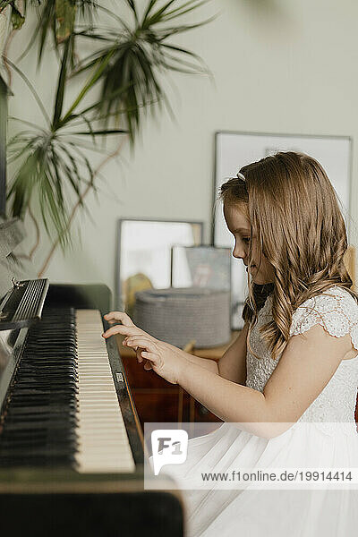 Girl wearing white dress and playing piano at home