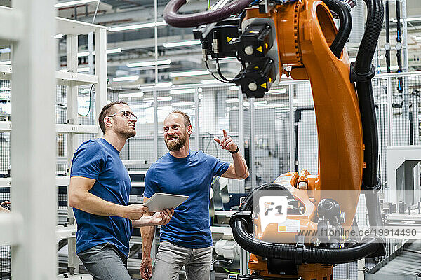 Two technicians with digital tablet examining industrial robot in a factory