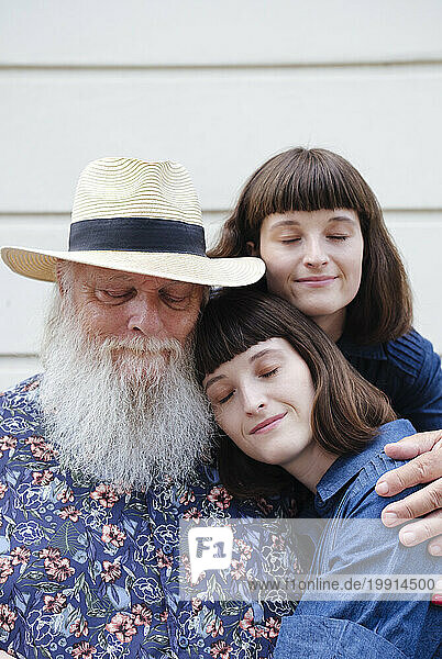 Father embracing daughters in front of wall
