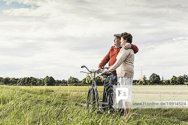Loving senior couple standing near bicycle under sky