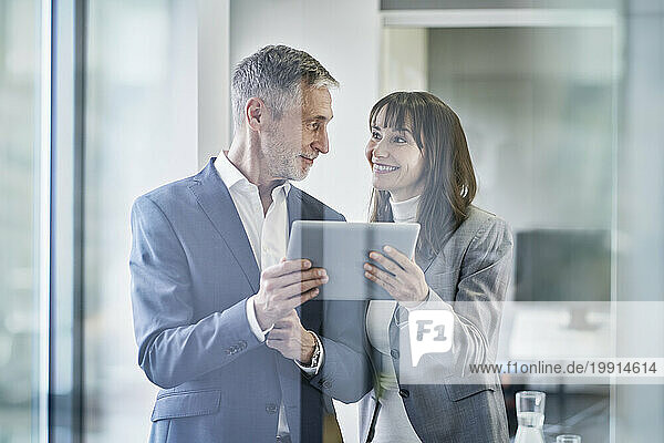 Happy businesswoman and businessman with tablet PC having discussion in office