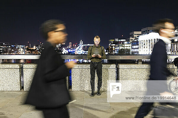 Man using smart phone standing near railing in city at night