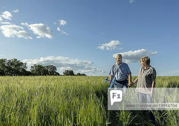 Senior couple holding hands walking in field under sky