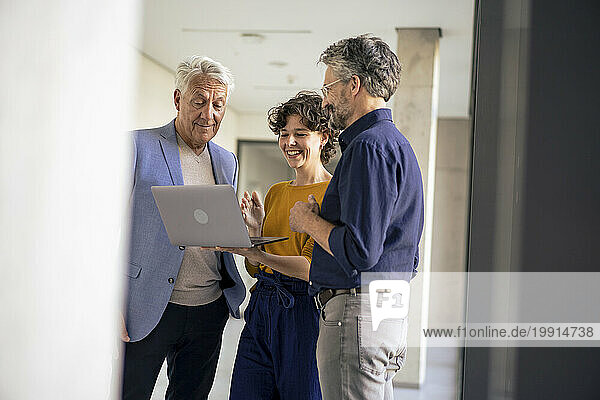 Happy business people having discussion over laptop in office corridor