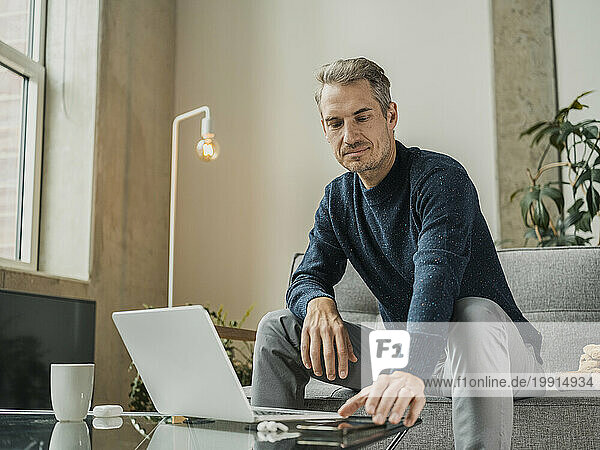 Freelancer sitting with smart phone and laptop at coffee table