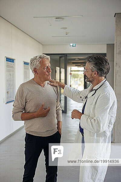 Doctor consoling man standing in hospital corridor