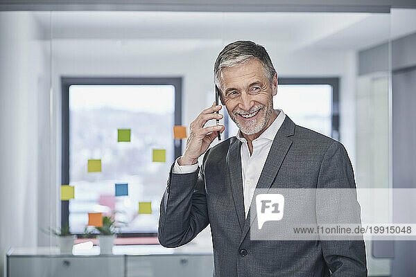 Happy senior businessman talking on smart phone in office
