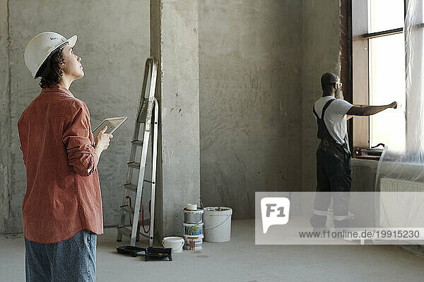 Engineer holding tablet PC with coworker looking through window at construction site