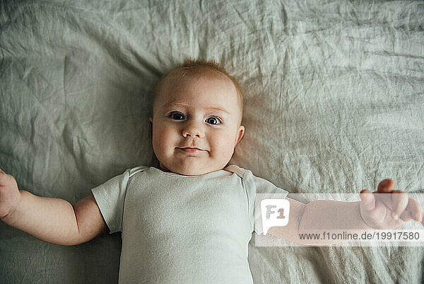 Overhead close up of baby laying on bed and smiling while reachi