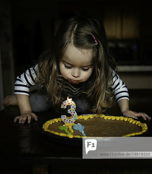 Cute little girl blowing out birthday candle in kitchen