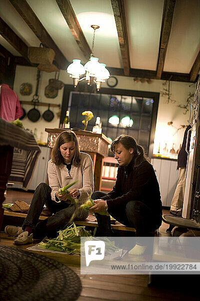 Two young women shuck corn for dinner during vacation in Stockbridge  Massechusetts
