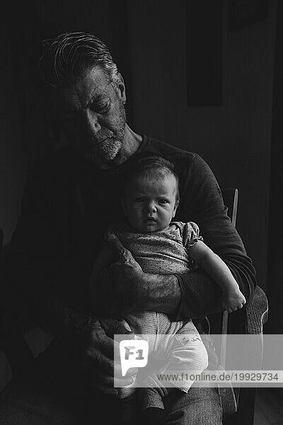 Newborn being held by Grandfather  both serious  black and white