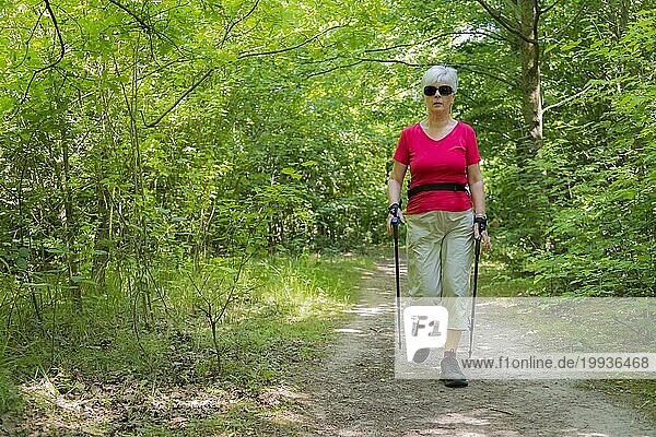 Eine ältere Dame beim Sport Nordic Walking auf einem Waldweg