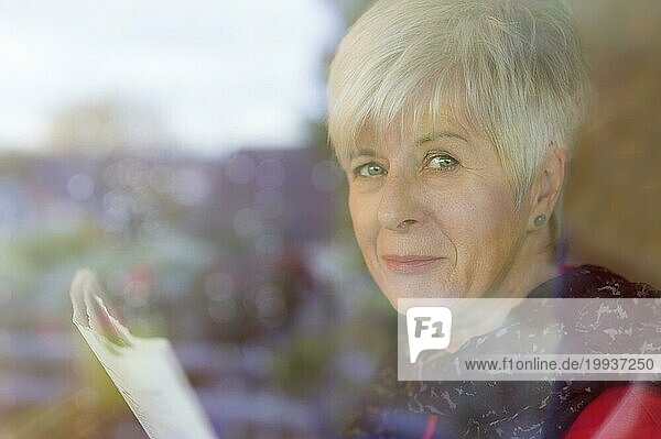 Ältere Dame sitzt hinter einer Glasscheibe und hält eine Zeitung in den Händen. Deutschland  Nordrhein-Westfalen  Grevenbroich