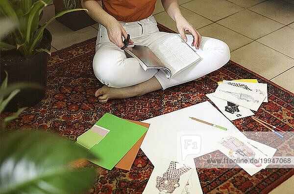 Junge Frau  die ihre Feng Shui Wunschkarten auf dem Teppich im Zimmer im Boho Stil mit vielen Pflanzen anlegt. Träume und Wünsche