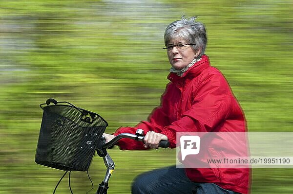ältere Dame in einer roten Jacke fährt schnell dirch den Wald