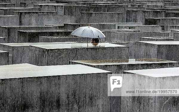 Ein Besucher des Denkmals für die ermordeten Juden Europas schützt sich mit einem Regenschirm vor starkem Regenfall. Berlin  23.06.2023