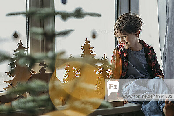 Smiling boy admiring Christmas decoration near window at home