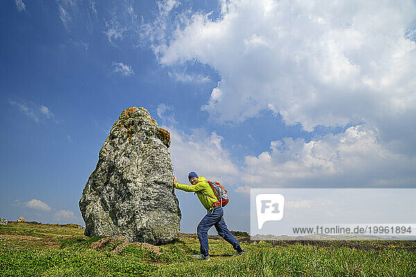 France  Brittany  Hiker pretending to push large menhir along Sentier Cotier route