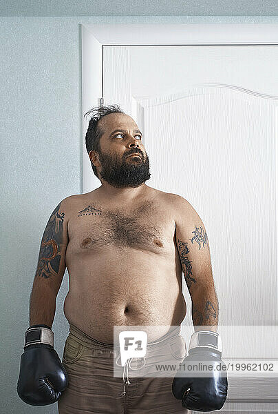 Mature overweight man wearing boxing gloves and standing at home