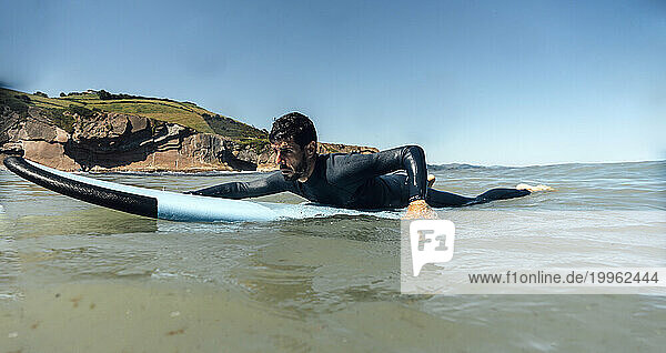Man with surfboard on sea under clear blue sky