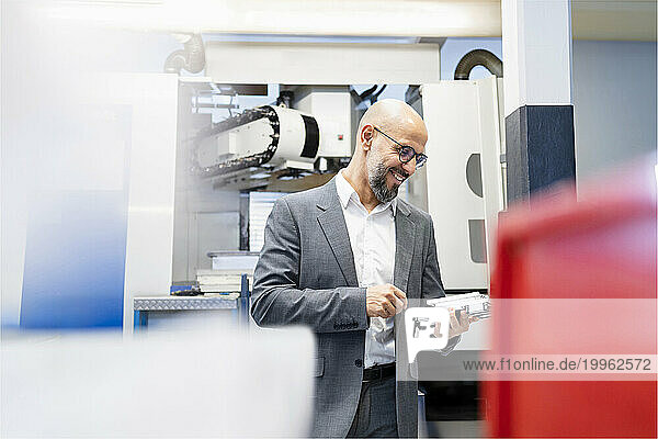Smiling businessman examining machine part in factory