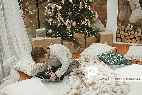 Boy playing with toy car on carpet near Christmas tree at home