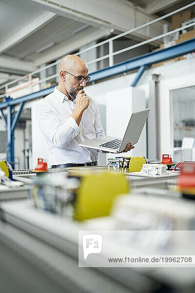 Businessman planning and using laptop near machinery in factory