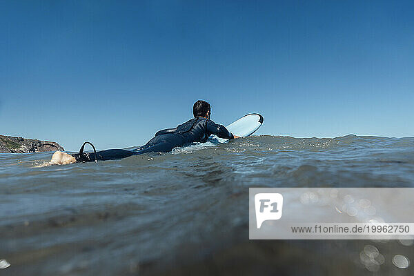 Surfer with surfboard on sea under clear blue sky