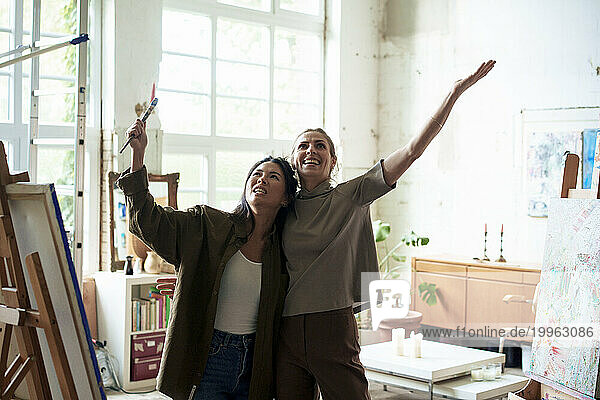 Happy women standing with arms raised in art studio
