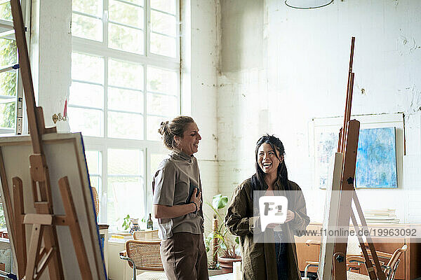 Happy women discussing over painting on easel in art studio
