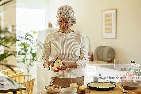 Mature woman peeling apples with knife at home