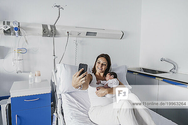 Mother taking selfie with baby girl in hospital
