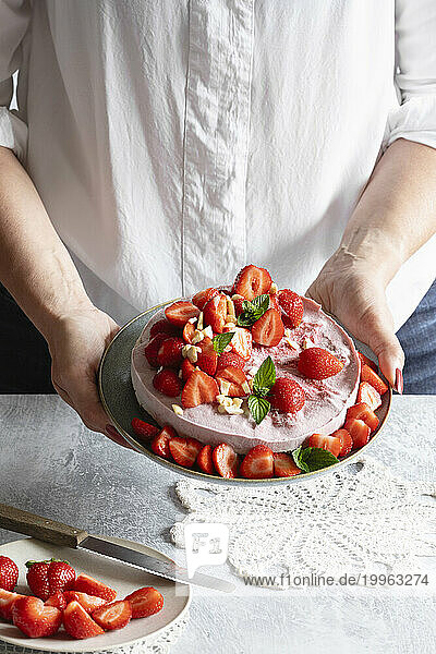 Hands of woman holding plate with ready-to-eat vegan strawberry tart