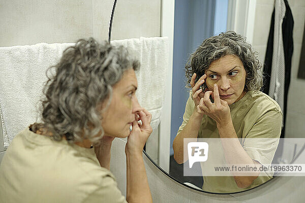 Woman applying under eye patches looking in mirror