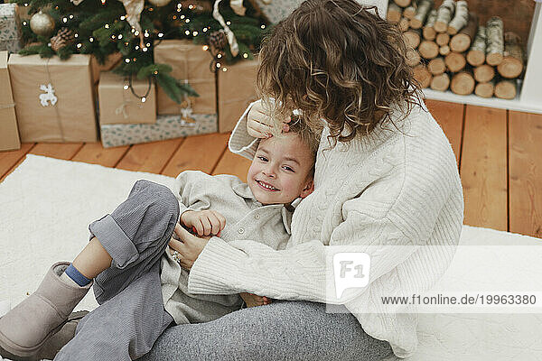 Mother embracing smiling son on white carpet at home