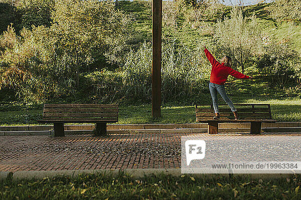 Woman standing on bench with arms outstretched in autumn park