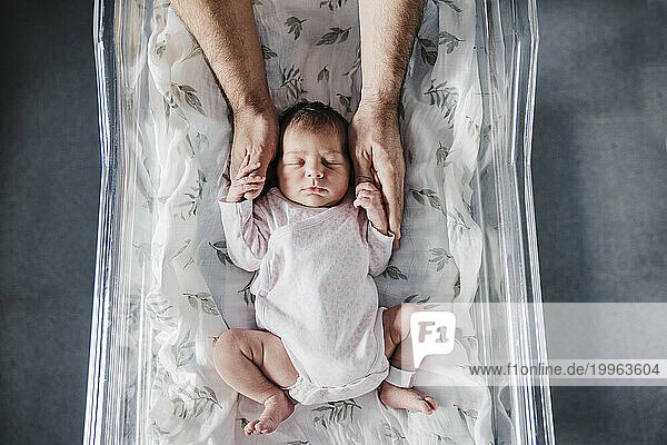 Father holding sleeping baby girl's hands in incubator