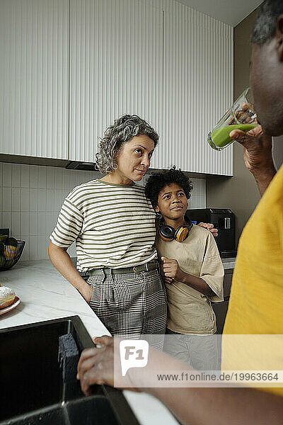 Mother and son looking at father drinking juice in kitchen
