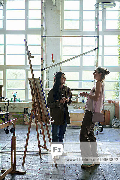 Woman and painter standing by easel in workshop