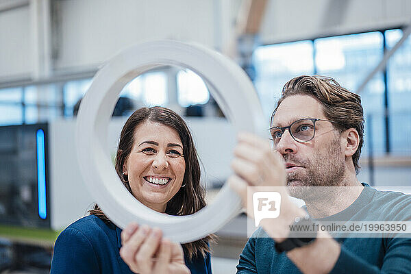 Happy businesswoman analyzing machine part with colleague in industry