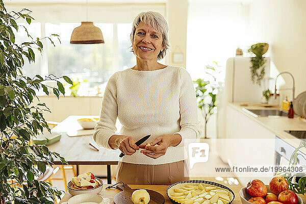Happy woman preparing apple pie in kitchen at home
