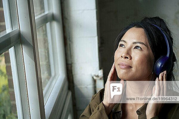 Smiling woman listening to music with headphones and looking out through window