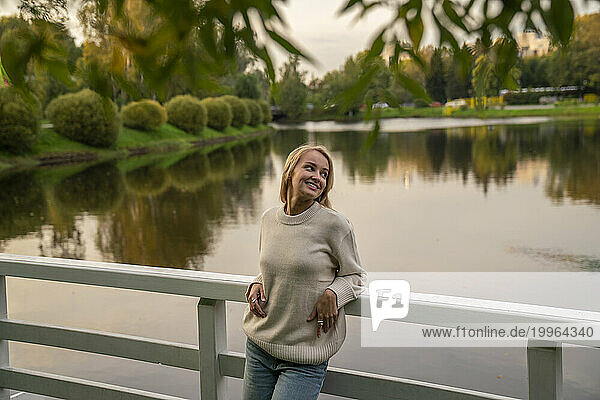 Smiling woman leaning on railing in front of lake at sunset