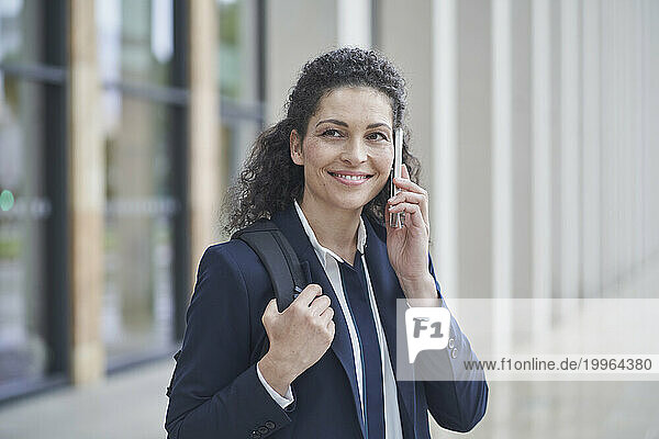 Happy businesswoman talking on smart phone near building