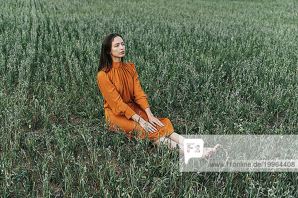 Thoughtful woman sitting amidst crops in corn field