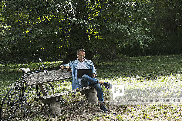 Man using laptop sitting on bench in park