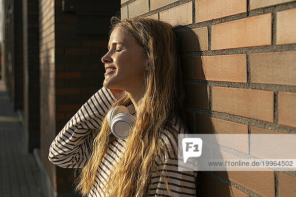 Blond woman with eyes closed in front of brick wall