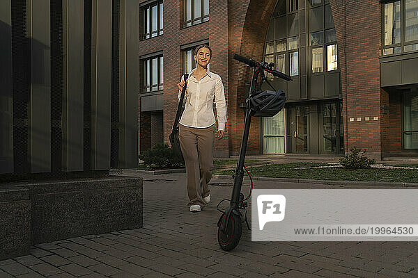 Businesswoman walking on footpath by electric push scooter
